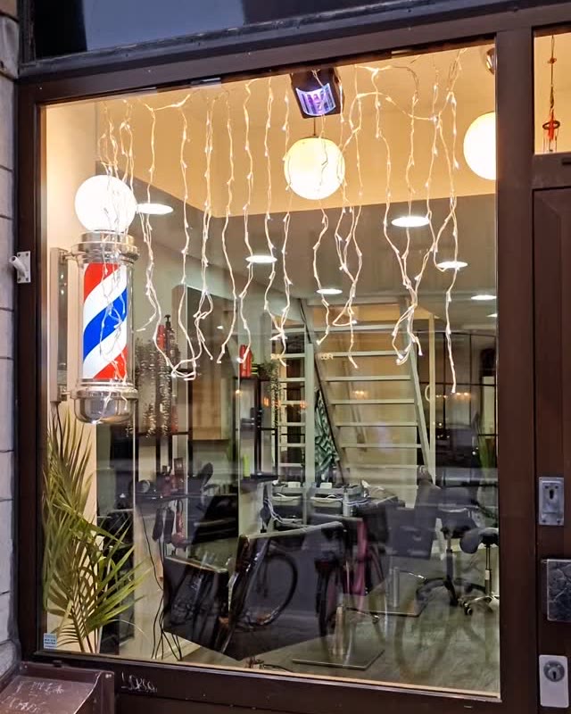 Ziad Barbershops skyltfönster på Hornsgatan en kväll, med tänd barberarstolpe